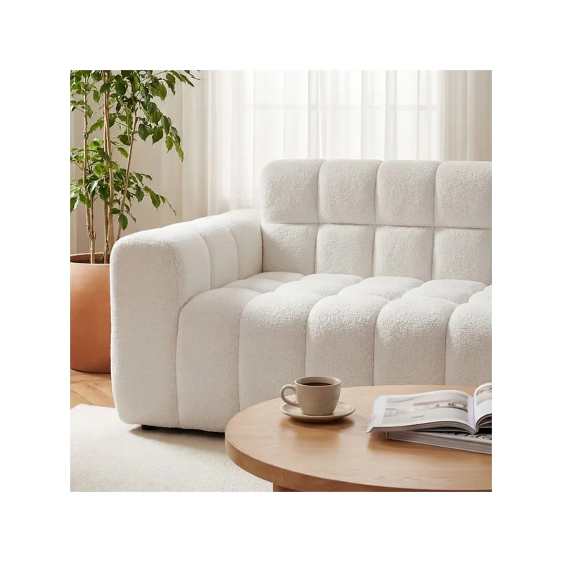 Close-up of the arm and the tufted seat of the white corner sofa, beside a coffee table