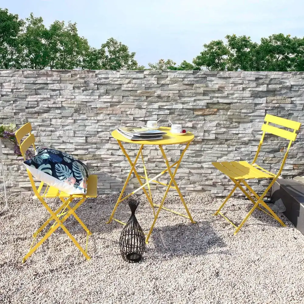 Yellow folding bistro set on gravel in front of a stone wall