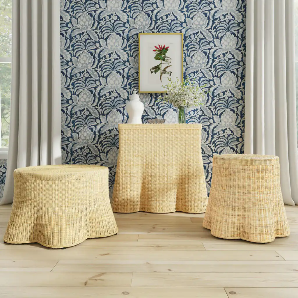 The round woven rattan coffee table shown with two other scalloped rattan pieces against patterned wallpaper