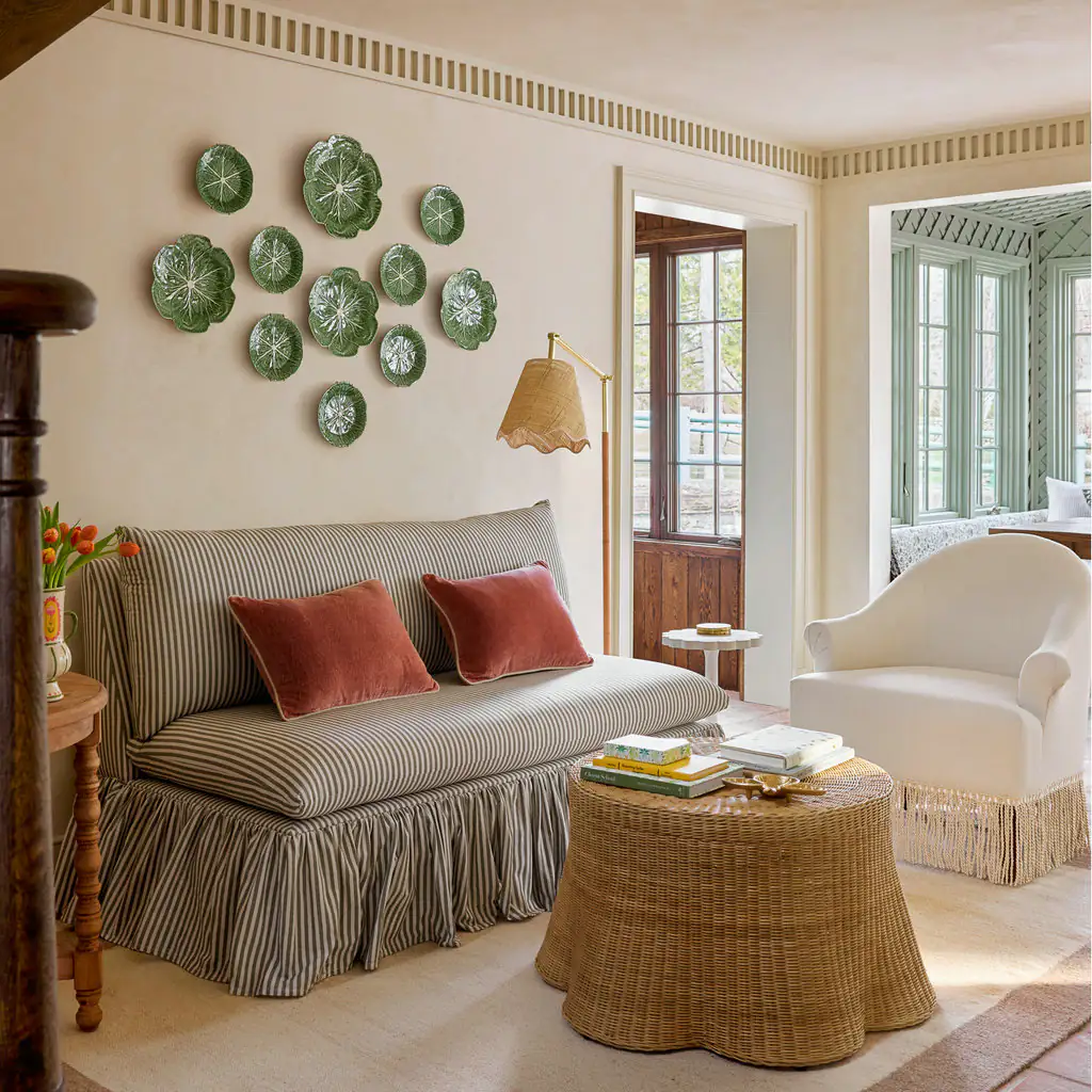 Round woven rattan coffee table in a living room with a striped sofa and green plates on the wall