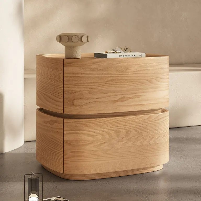Curved two-drawer bedside table in a natural wood finish, with a vase and books on top