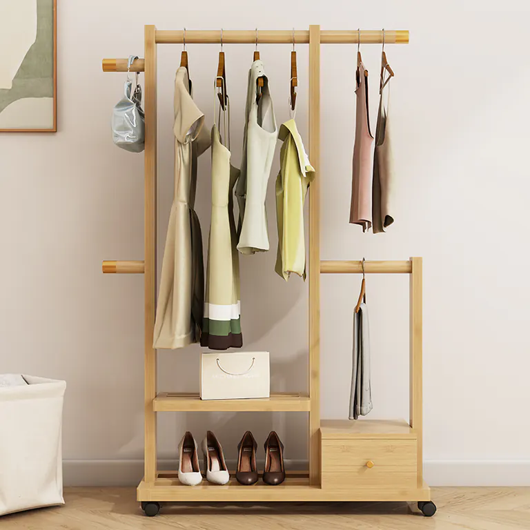 Clothes rack in a light wood finish holding clothes and shoes, with a small drawer, against a pale wall